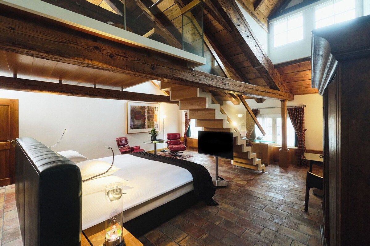 Ein geräumiger Raum mit einem großen Bett, einem Schreibtisch, einem Stuhl, einem Fernseher und einer Treppe zu einer oberen Ebene.