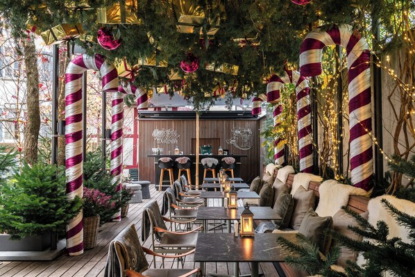 Un espacio al aire libre acogedor con mesas y sillas, rodeado de decoraciones festivas y follaje.