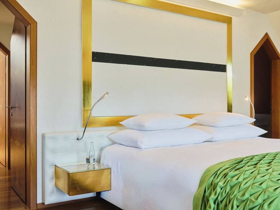 A hotel room with a bed, a bedside table with a bottle, and a green throw blanket.