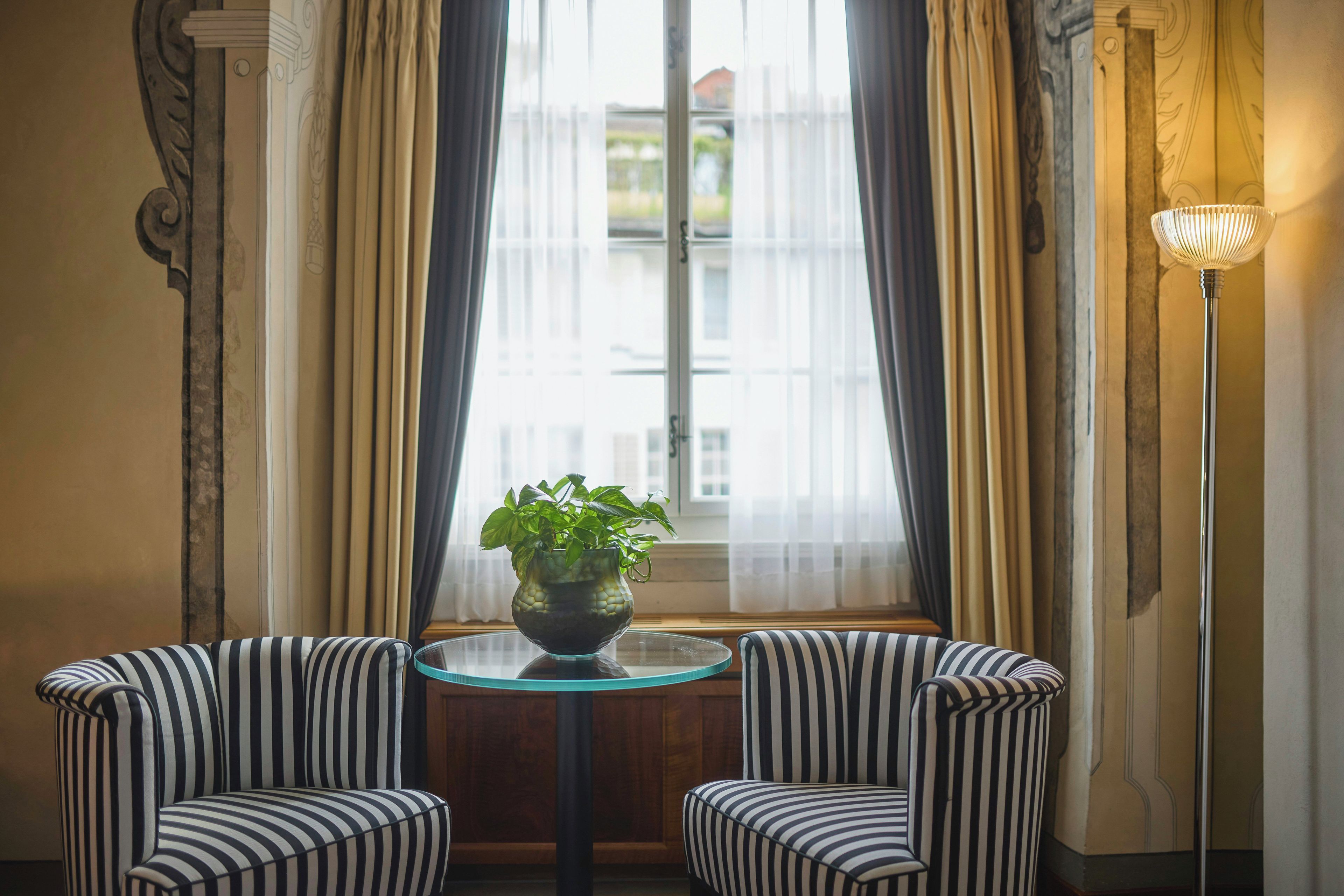 A room with two striped armchairs, a round glass table with a plant, and a floor lamp.