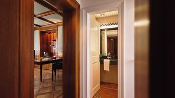 Un pasillo con una puerta de madera que da a un comedor con una mesa y sillas, y una cocina con un fregadero y encimera visibles a través de una puerta abierta.