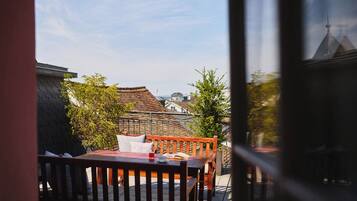 A balcony with a wooden table and chairs, a potted plant, and a view of traditional buildings.