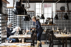 Un restaurante con paredes de baldosas blancas y negras en damero, mesas de madera y lámparas colgantes.