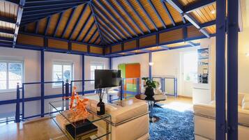 A modern living room with a glass coffee table, a flat-screen TV, and a blue carpet.