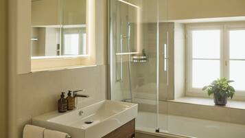 A bathroom with a glass shower enclosure, a large mirror, and a vanity with a sink and soap dispensers.