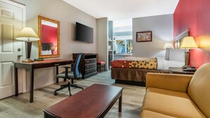 Quarto de hotel com escrivaninha, cadeira, cama e televisão.
