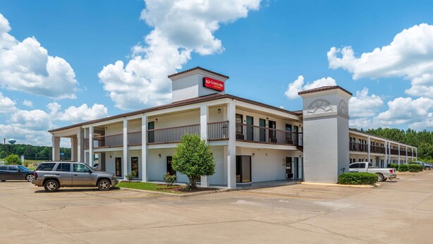 A motel with a two-story structure, a covered parking area, and a small tree in front.