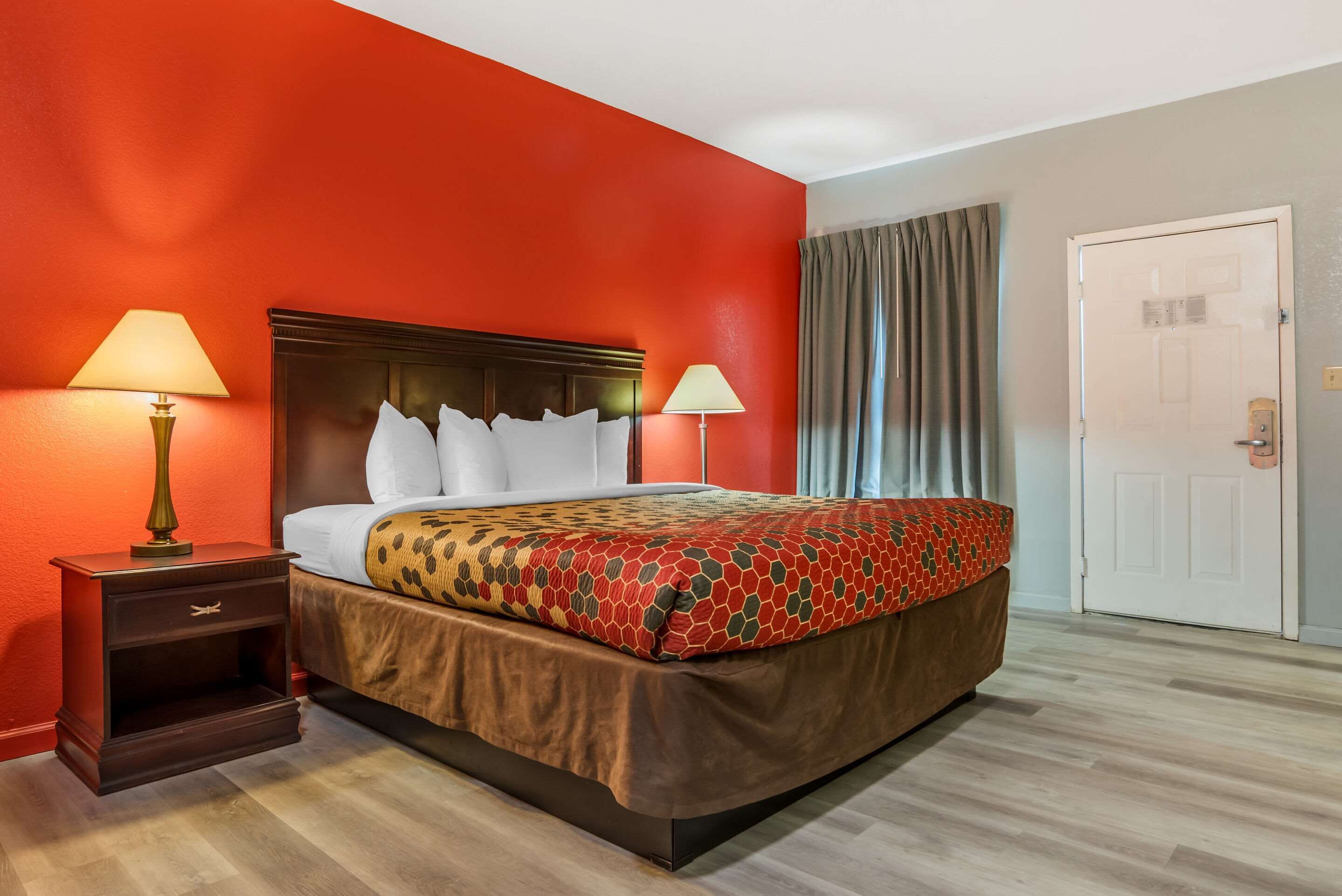 A hotel room with a large bed, two bedside lamps, a wooden nightstand, and a door.