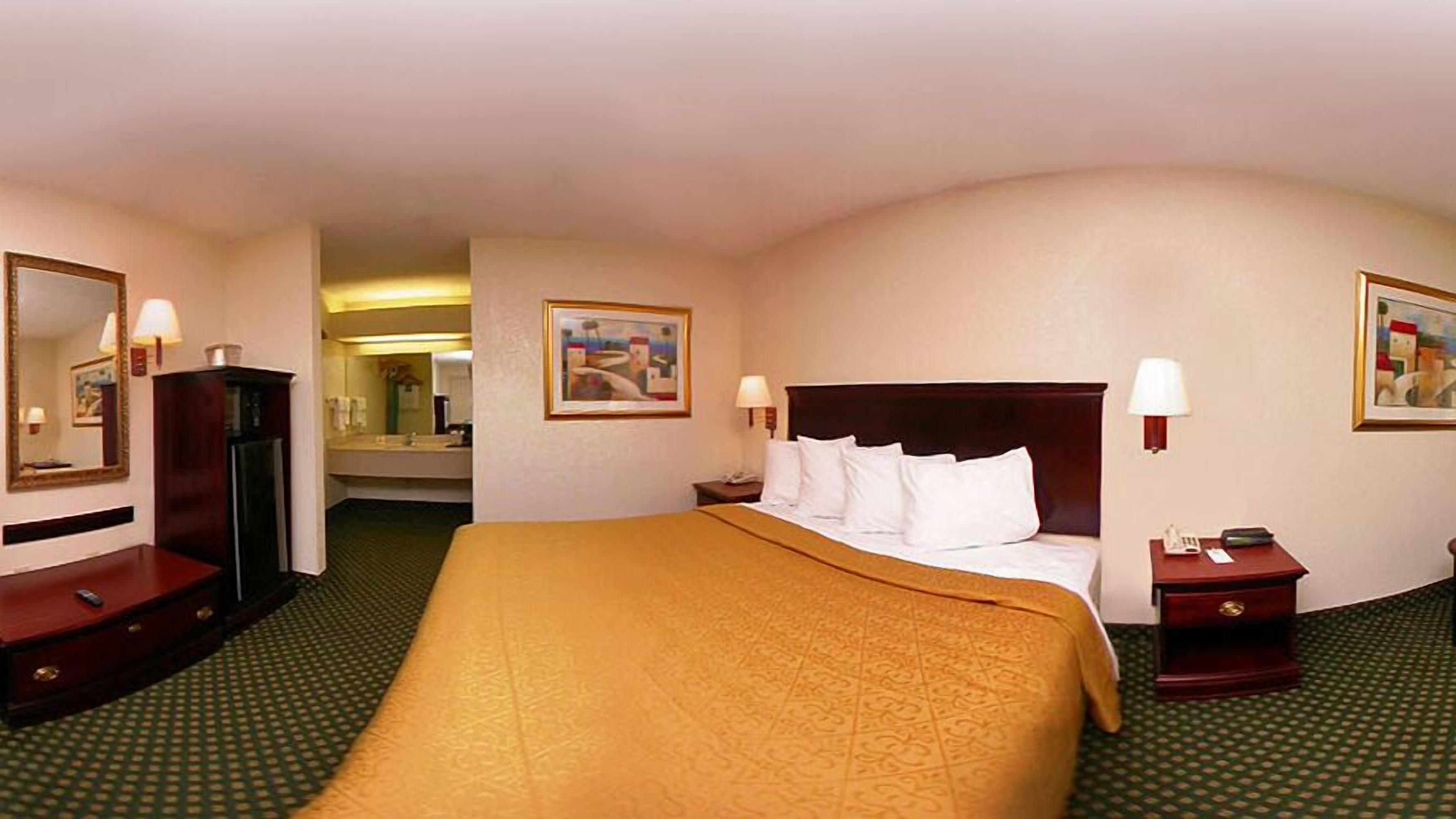 Un cuarto de hotel con una cama grande, un tocador, un espejo, una mesita de noche y un cuadro en la pared.