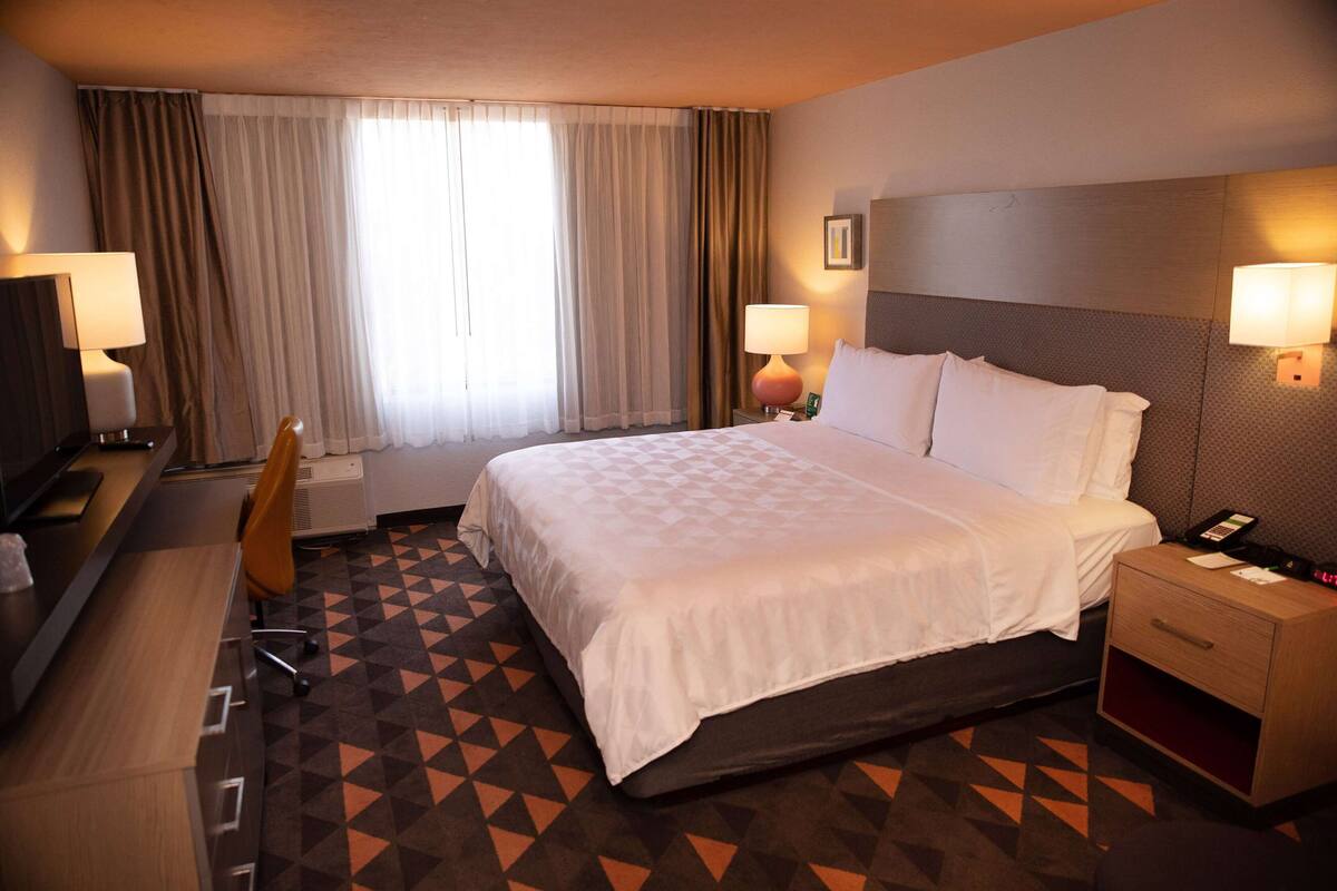 A hotel room with a large bed, a desk with a chair, a TV, and a lamp.