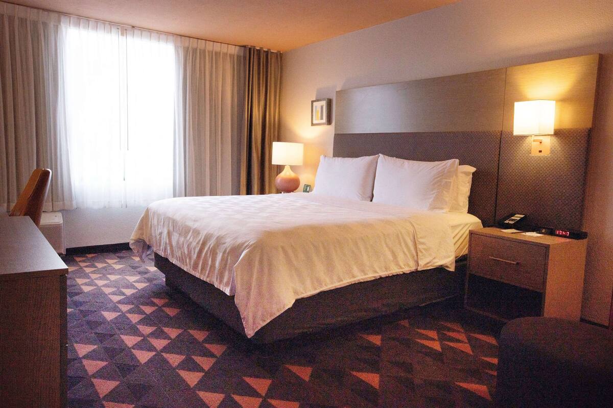 A hotel room with a large bed, two bedside lamps, a desk, and a chair.