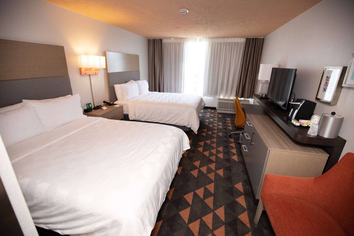 A hotel room with two beds, a desk with a TV, and a bathroom.