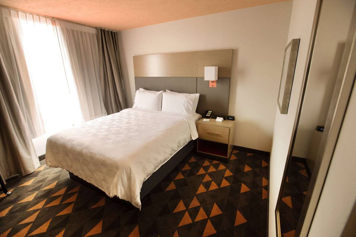 A hotel room with a bed, a nightstand, a wall-mounted lamp, and a patterned carpet.