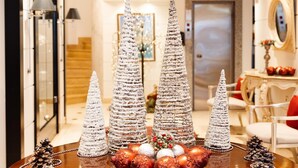 Uma mesa de madeira redonda com um arranjo decorativo que inclui ornamentos prateados e vermelhos, pinhas e uma tigela.