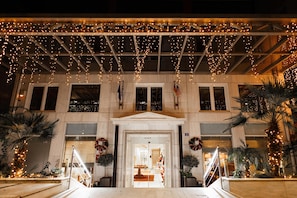 A building entrance with a covered walkway adorned with string lights, palm trees, and wreaths.