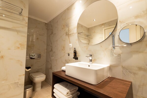 A modern bathroom with a marble wall, a white sink, a round mirror, and a toilet.