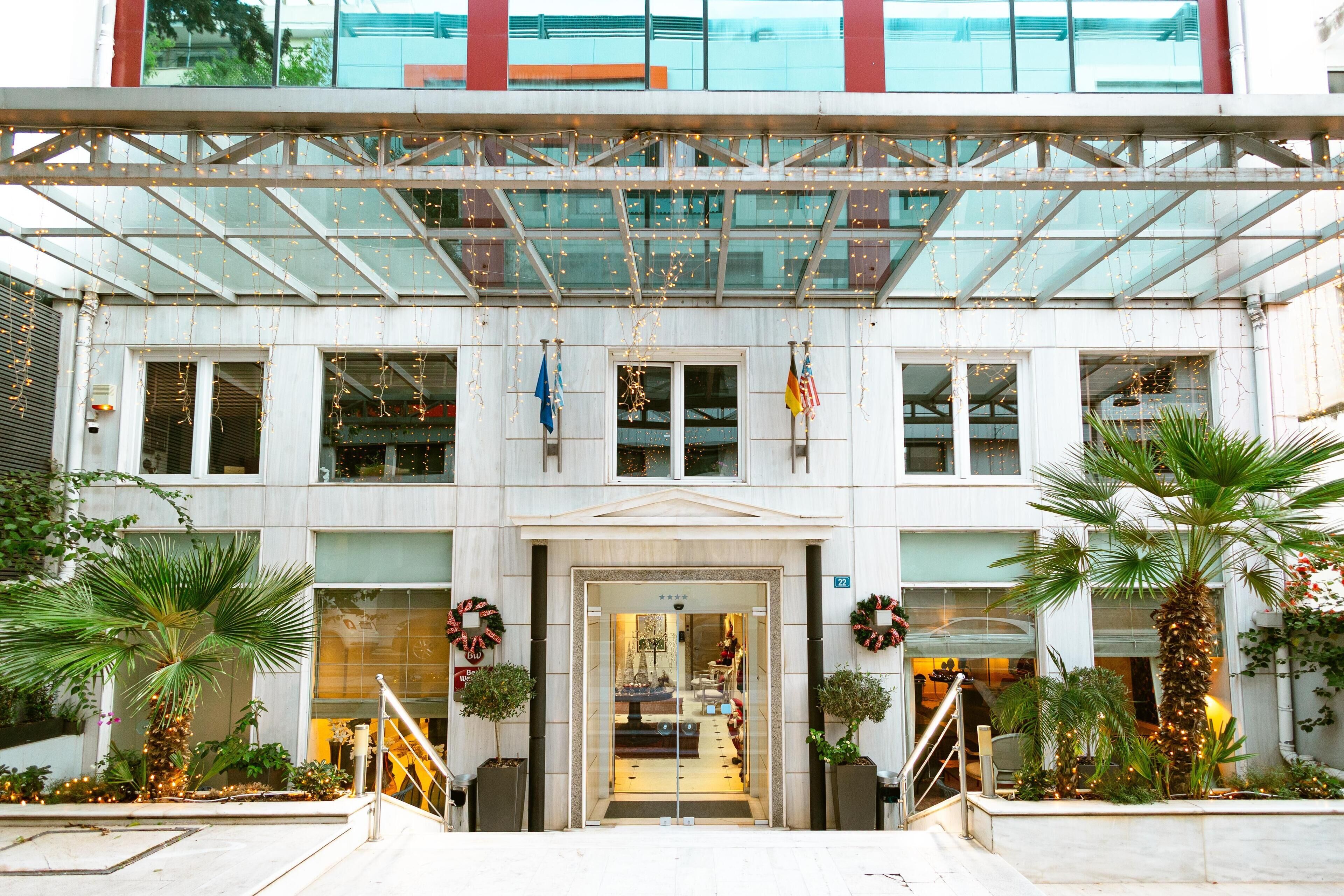 A hotel entrance with a glass canopy, palm trees, and holiday wreaths.