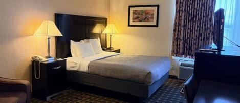 A hotel room with a bed, two bedside lamps, a telephone, a desk, a chair, and a window with curtains.