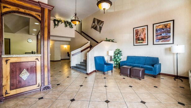 Un hall d’entrée spacieux avec un canapé bleu, un comptoir d’accueil en bois, un escalier et deux lampes fixées au mur.