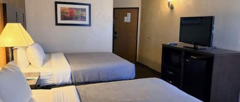 Habitación de hotel con dos camas, un televisor, una lámpara y un cuadro en la pared.