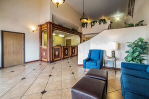Welcome to our lobby, featuring a spacious area with a high ceiling and a geometric patterned floor. Guests can relax in comfortable armchairs and enjoy the natural surroundings.