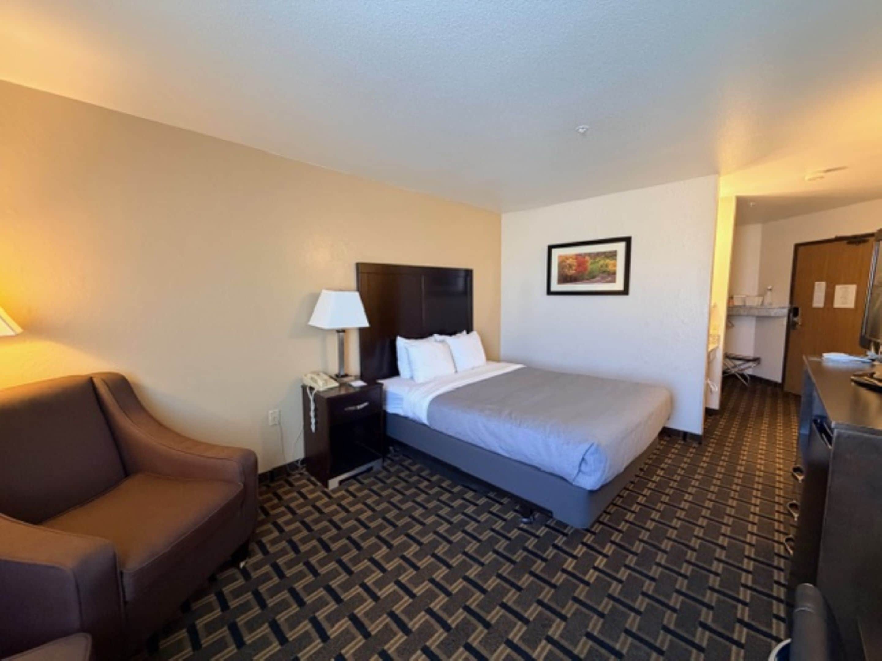 Una habitación de hotel con una cama, una mesita de noche, una lámpara, una silla y un escritorio.