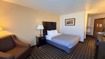 Una habitación de hotel con una cama, una mesita de noche, una lámpara, una silla y un escritorio.
