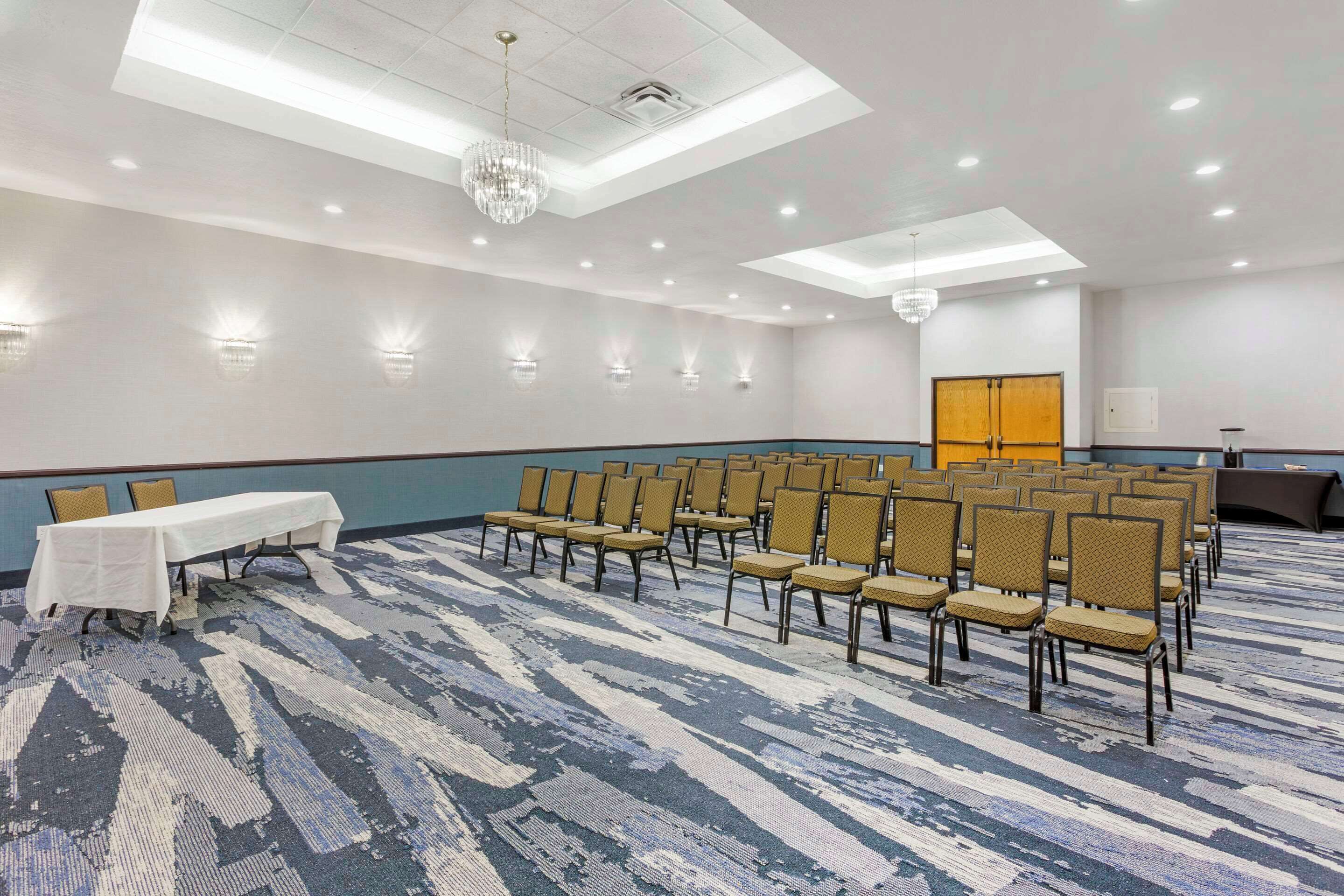 Uma sala de conferências com uma mesa comprida e fileiras de cadeiras, um candelabro e iluminação embutida.