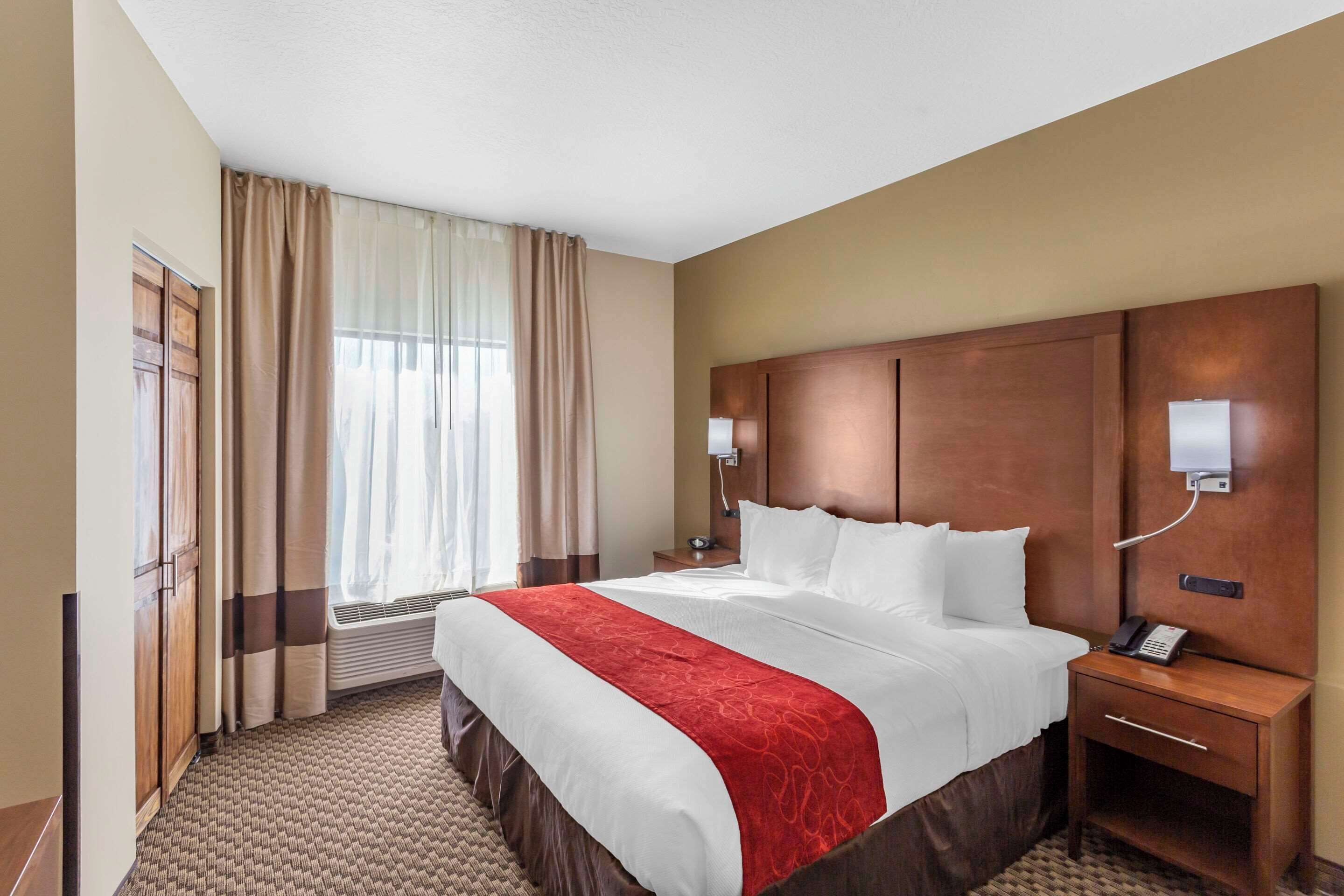 A hotel room with a large bed, a wooden headboard, a bedside table with a phone, and a window with curtains.