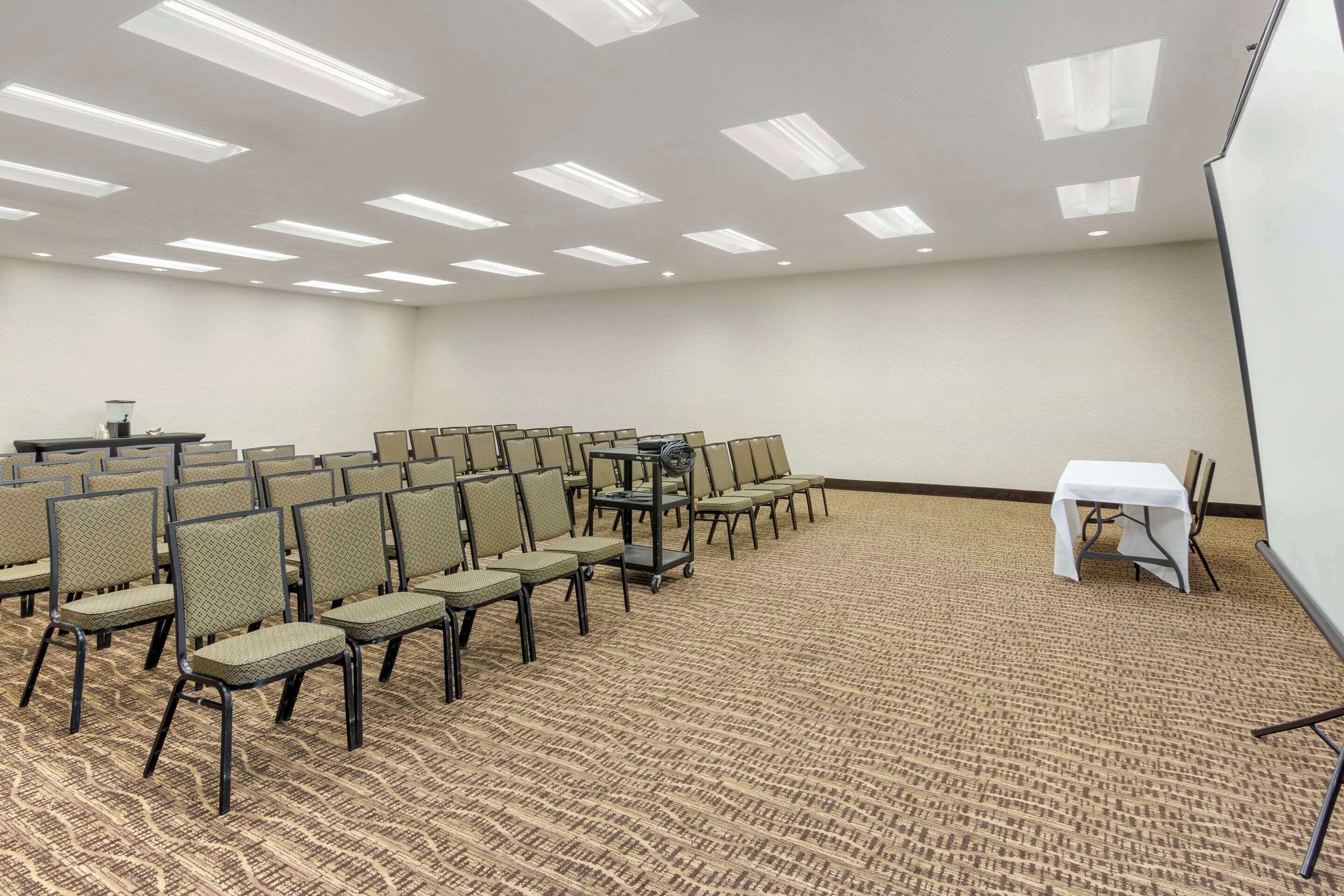 A conference room with rows of chairs, a projector screen, and a white table.
