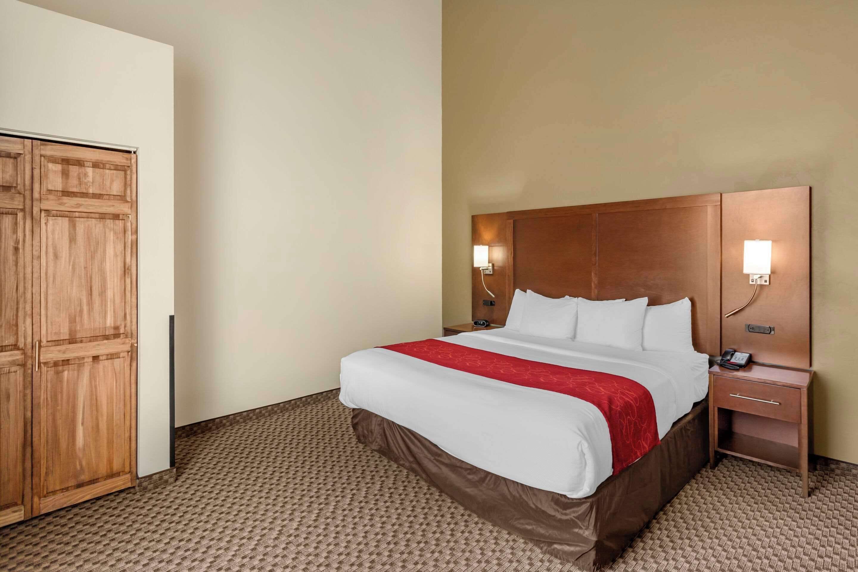 A hotel room with a large bed, wooden wardrobe, bedside tables with lamps, and a carpeted floor.