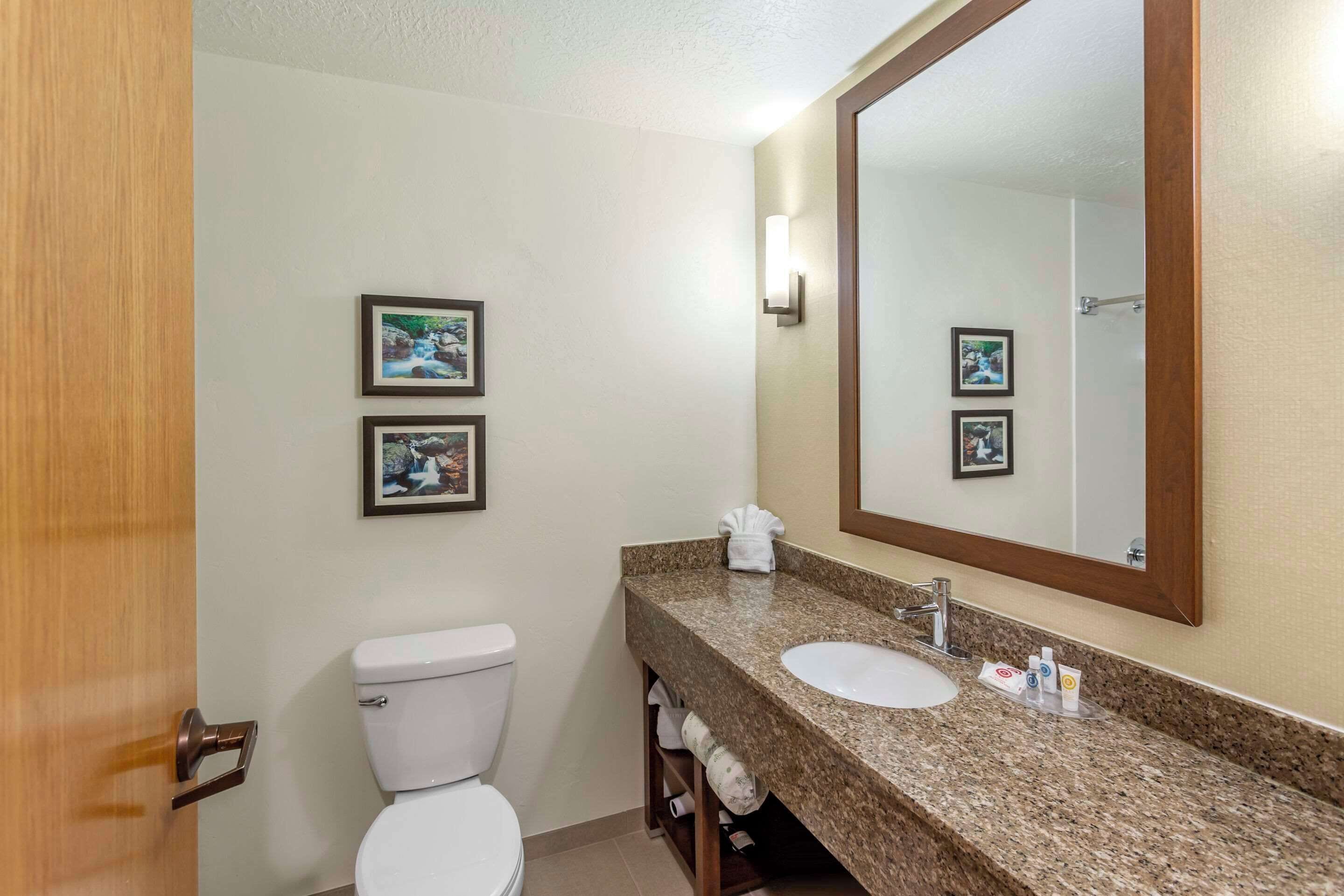 A bathroom with a toilet, sink, and mirror. There are framed pictures on the wall.