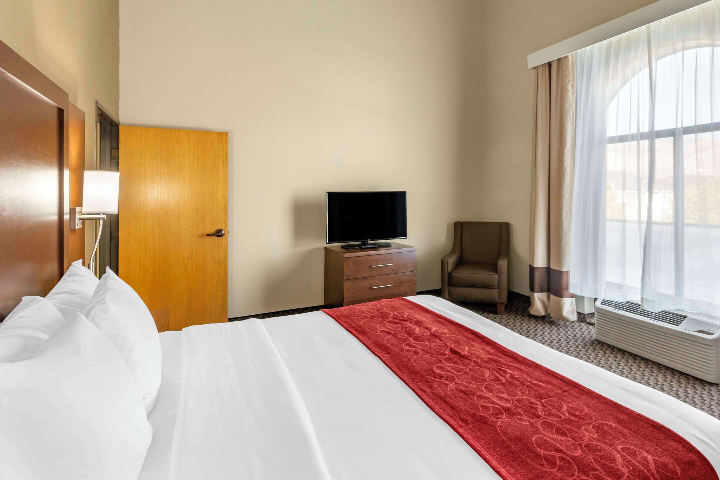 Een hotelkamer met een bed, een televisie, een stoel, een bureau en een raam met gordijnen.