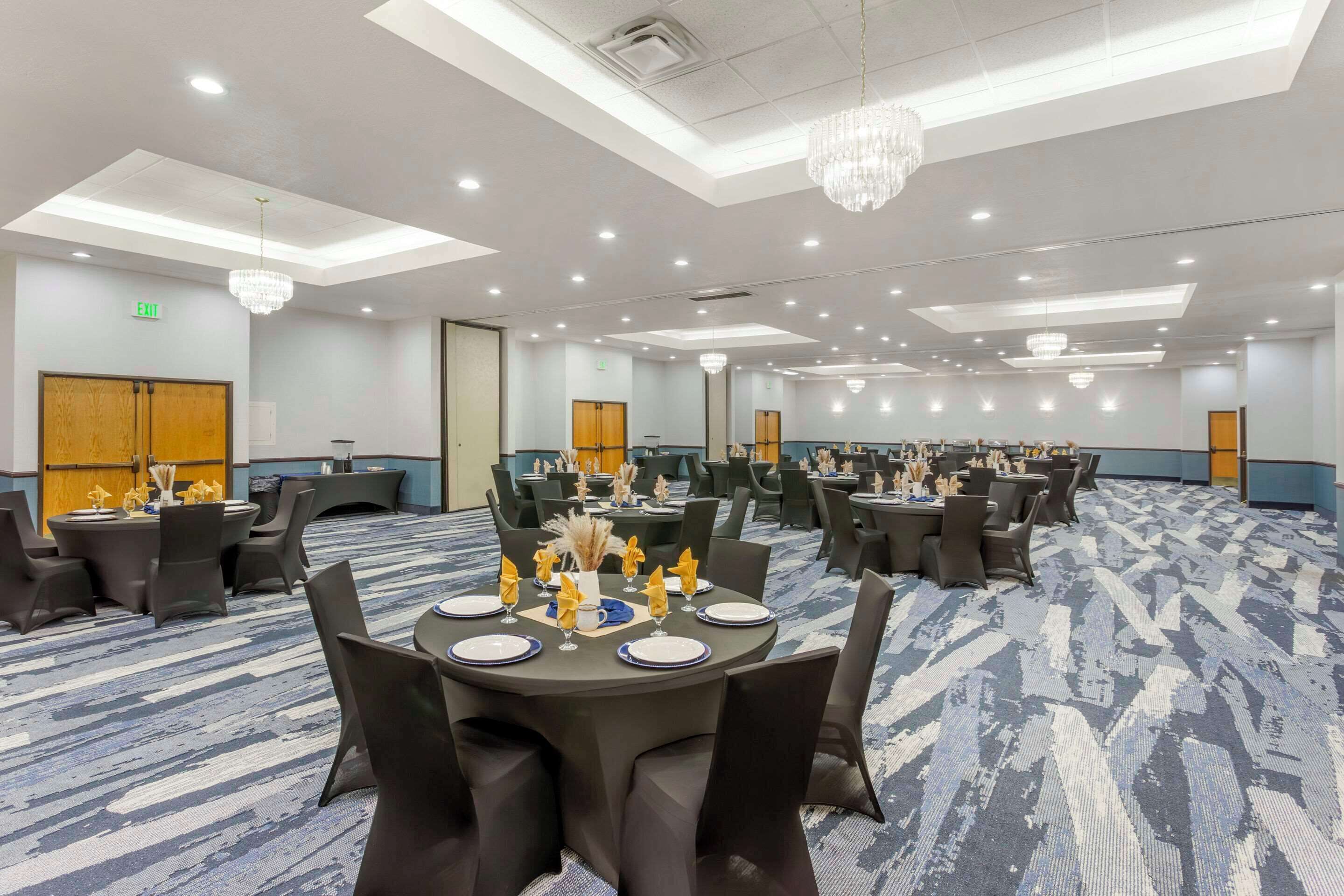 Un salón de conferencias con mesas redondas, sillas negras y candelabros.