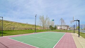 An outdoor basketball court with a green playing surface and a red surrounding area.