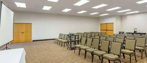 Uma sala de conferências com fileiras de cadeiras, uma tela de projetor e um palanque.