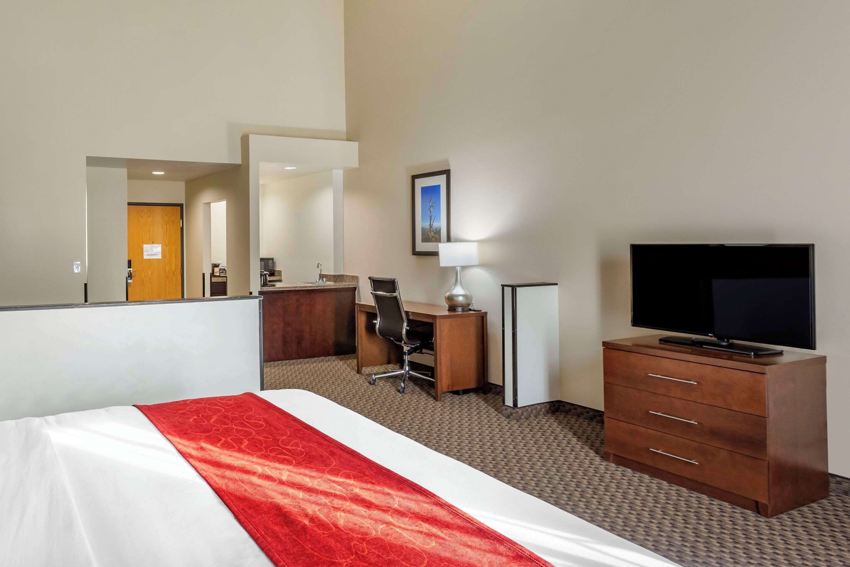Una camera d'albergo con un letto, una scrivania, una sedia, una televisione e un comò.