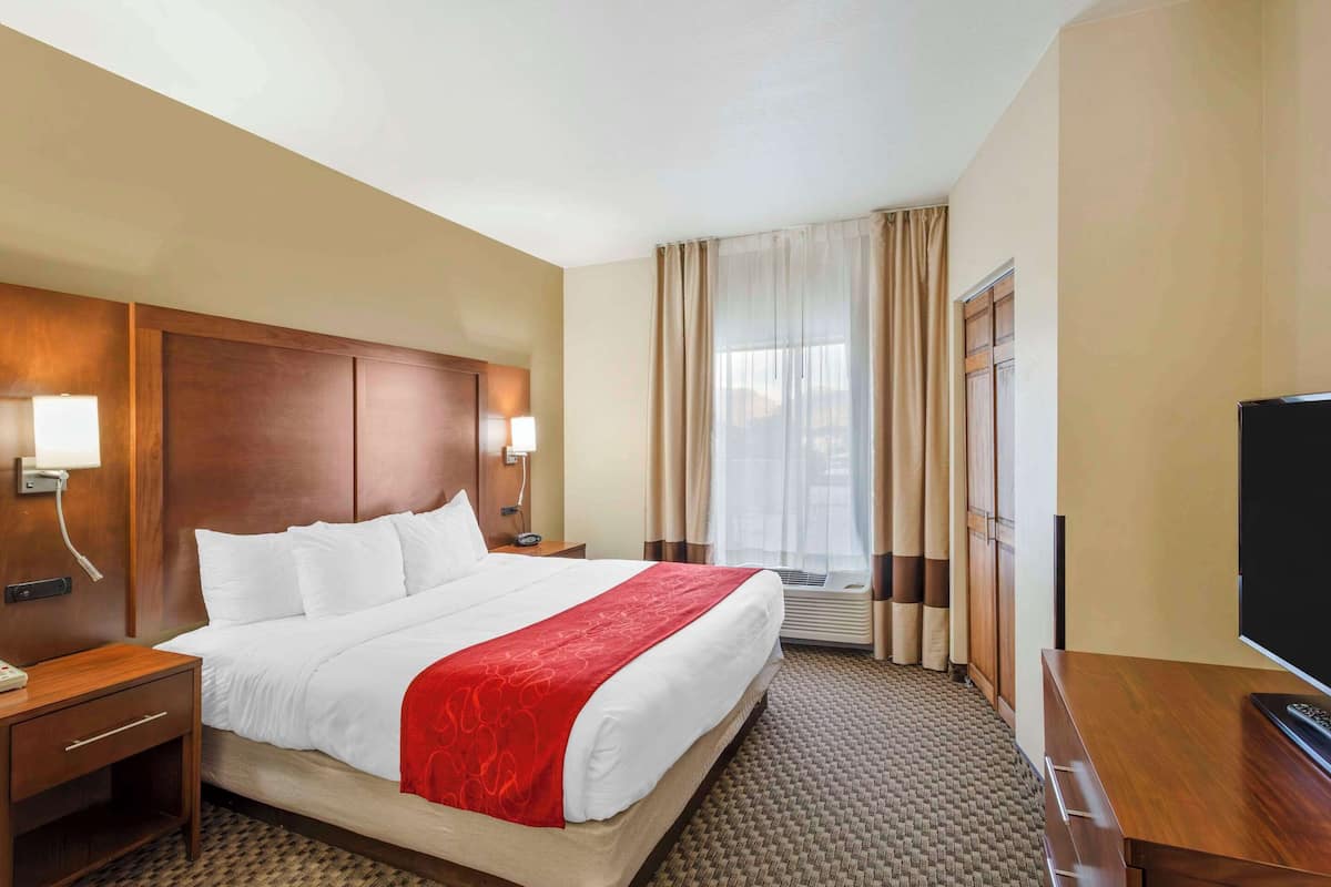 Ein Hotelzimmer mit einem großen Bett, einem hölzernen Kopfteil, einem Fernseher, einem Schreibtisch und einem Fenster mit Vorhängen.