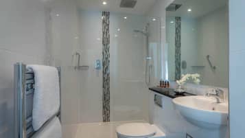 Un baño moderno con ducha de vidrio, inodoro blanco y lavamanos con espejo.