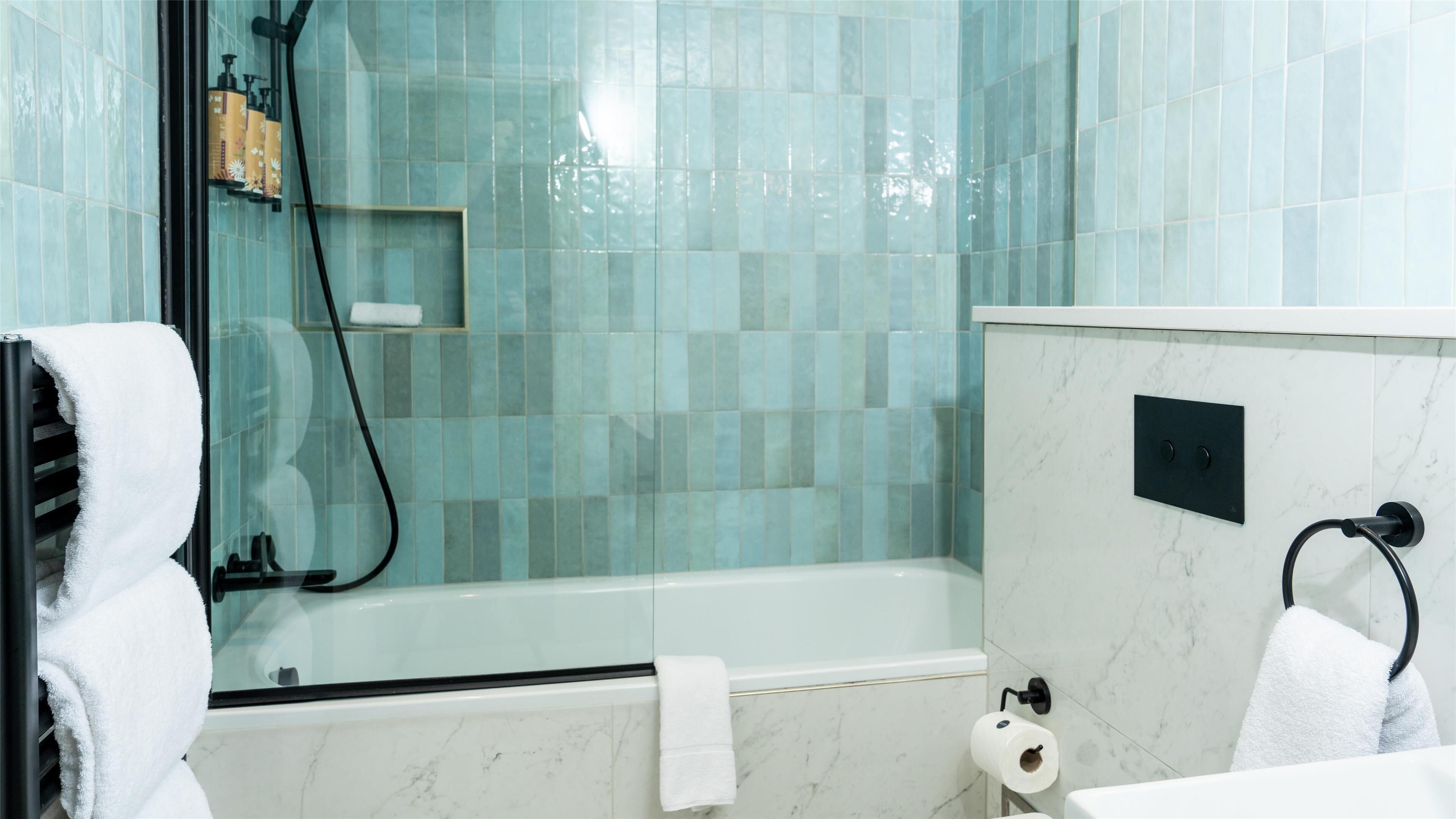 A bathroom with a glass-enclosed shower, a white bathtub, and a marble-tiled wall.