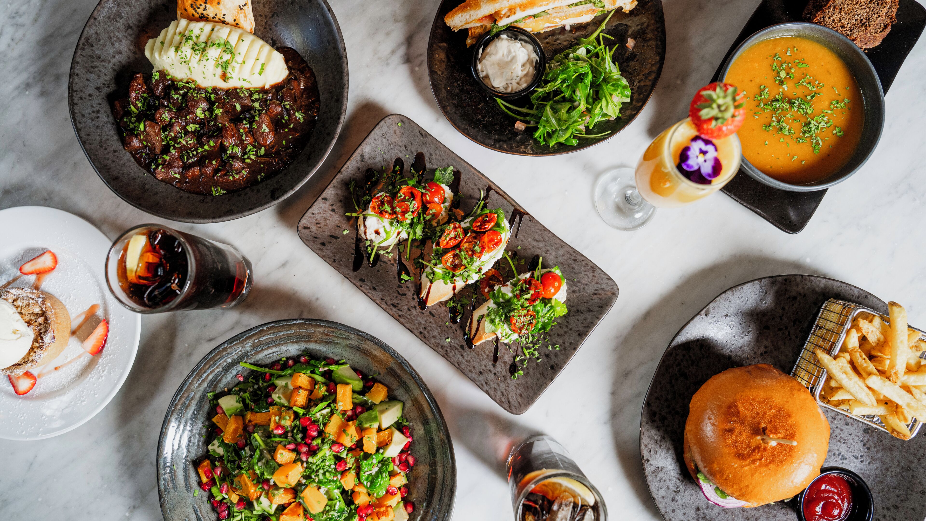 A variety of dishes including a burger, fries, a salad, and a bowl of soup.