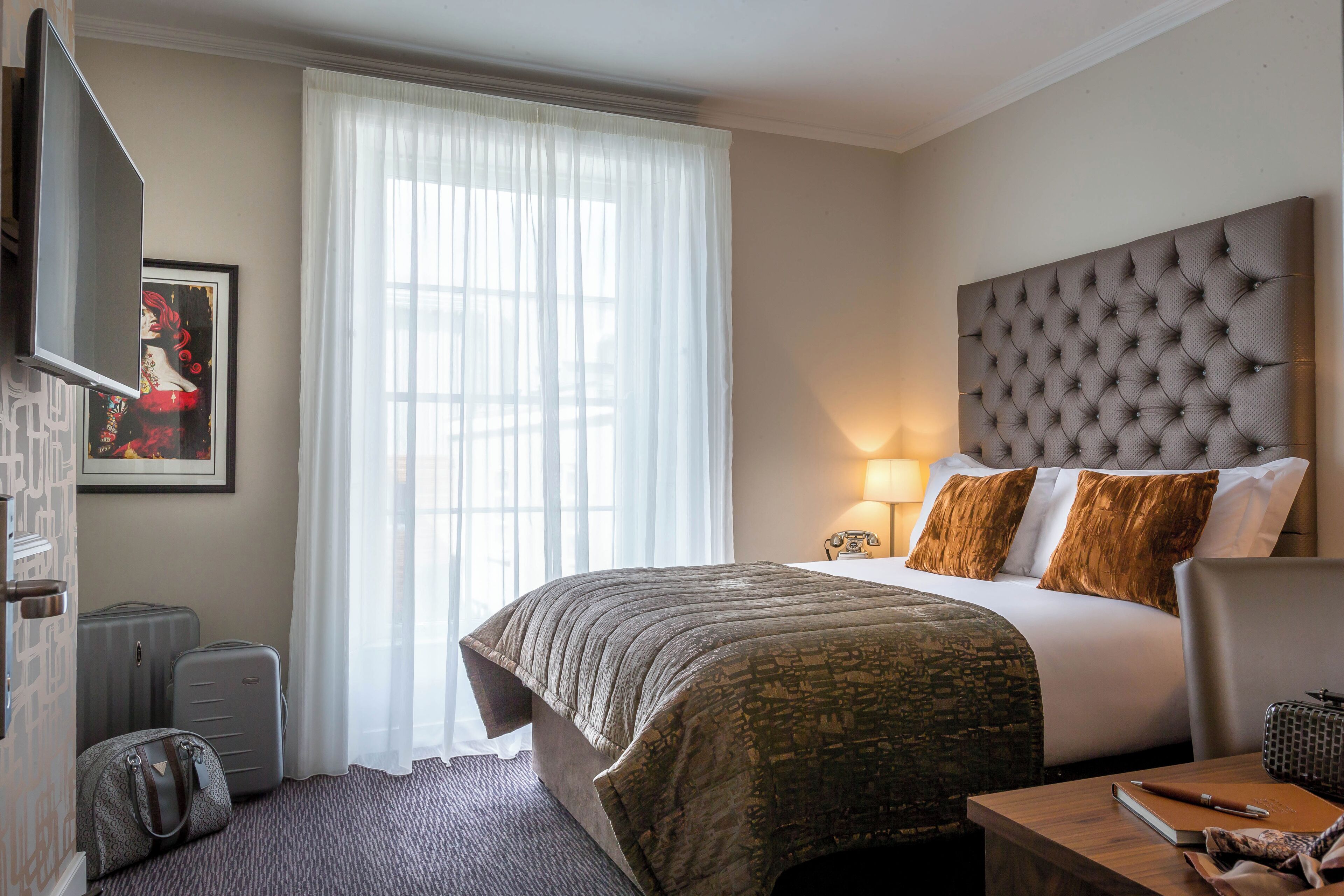 Une chambre d’hôtel équipée d’un lit, d’un bureau, d’une chaise, d’une télévision, d’une lampe et d’une fenêtre avec des rideaux.