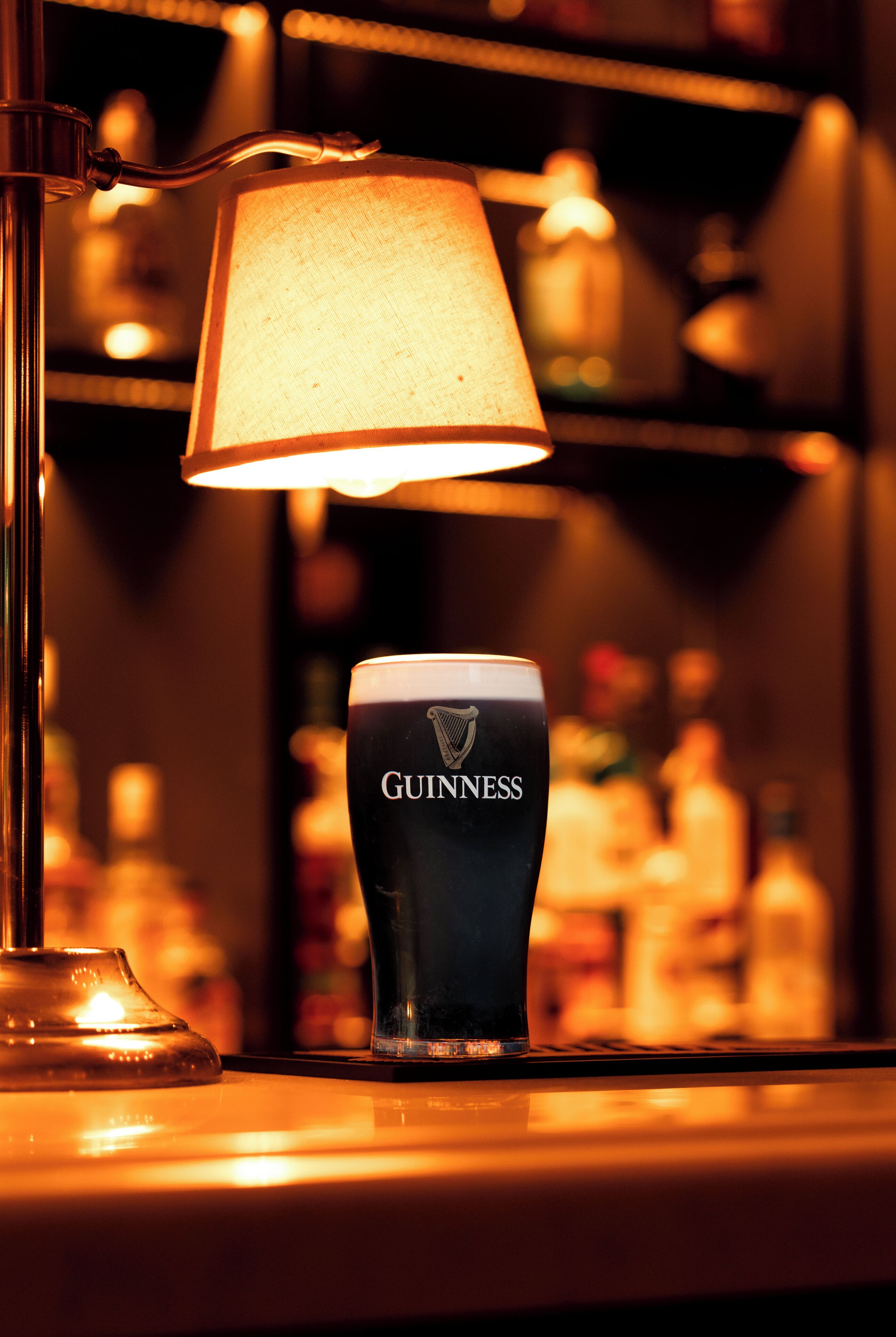 A glass of Guinness beer on a bar counter with a lamp in the background.