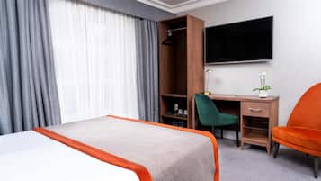 Una habitación de hotel con cama, escritorio con silla, televisor y una planta.