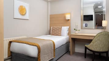 A hotel room with a bed, a desk, a chair, a bedside table, a lamp, a mirror, and a framed picture on the wall.
