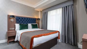 Una habitación de hotel con una cama grande, una mesita de noche, una lámpara de pared y un ventanal con cortinas.