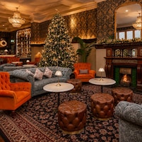 A cozy lounge area with a Christmas tree, plush seating, and a fireplace.