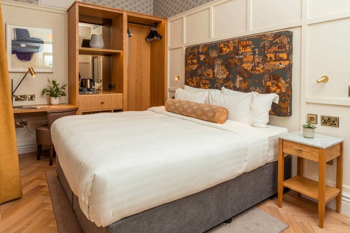 Un dormitorio con una cama grande, un escritorio con una silla, un armario y una mesita de noche con una lámpara.