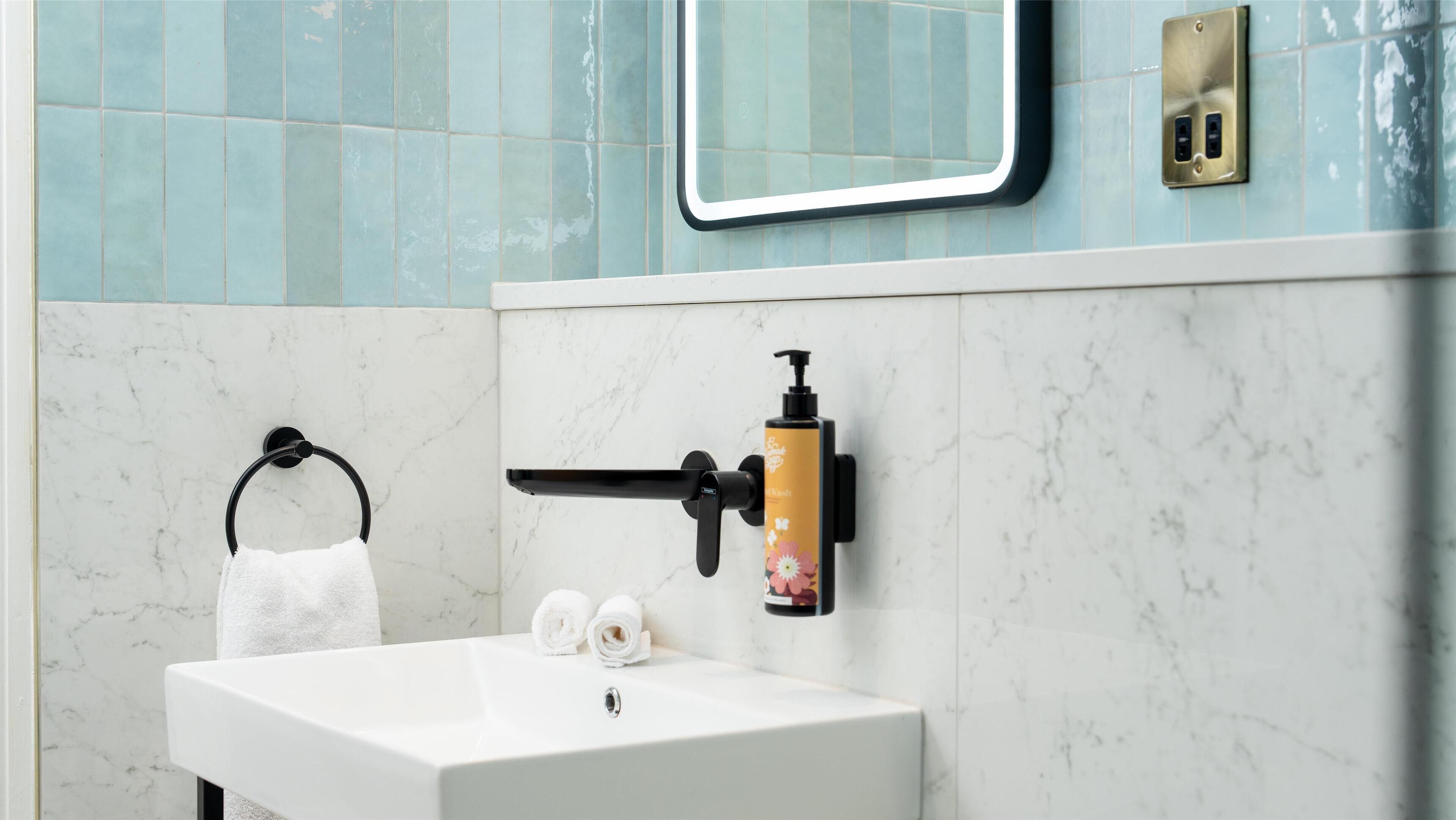 A bathroom with a white sink, a towel ring, a mirror, and a soap dispenser mounted on the wall.