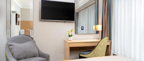 Habitación de hotel con cama, escritorio, silla, televisor y espejo.